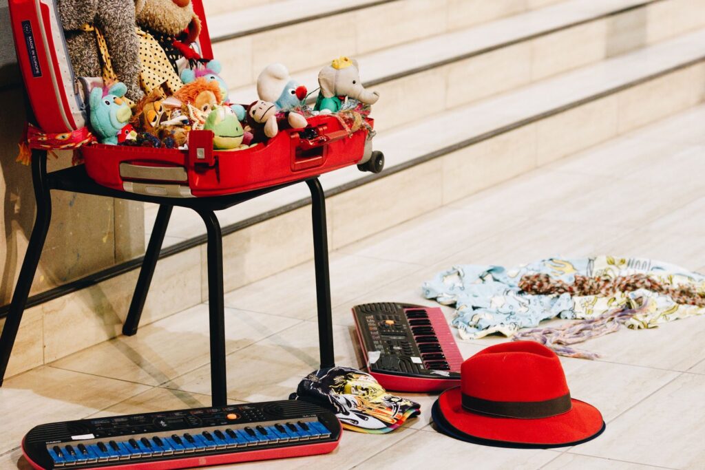 Plush toys in a suitcase on a chair, with an electronic organ and some hats on the floor.