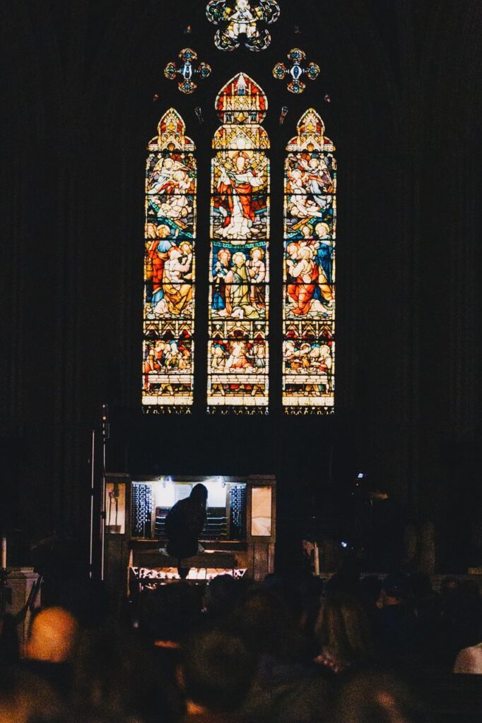 Three beautiful stained glass windows above a woman playing an organ in church.